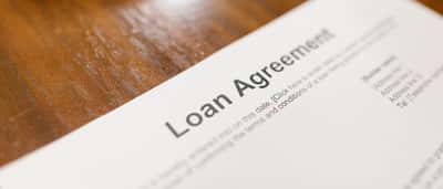 A close-up view of a detailed loan agreement document resting on a wooden desk.