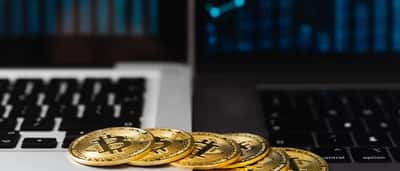 Gold Bitcoin tokens sit on a laptop keyboard in front of a screen displaying a financial chart.