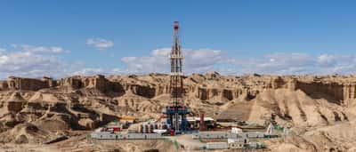 An active oil drilling rig surrounded by facilities in a vast, arid, rocky desert landscape.