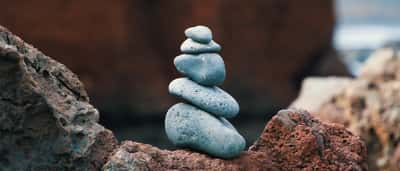 A stack of smooth, blue-grey stones carefully balanced on a textured red rock.