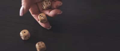 A hand rolling three wooden dice onto a dark surface in moody, dramatic lighting.