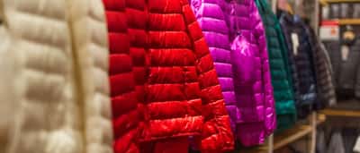 Brightly colored winter jackets hang on a clothing rack in a retail store.