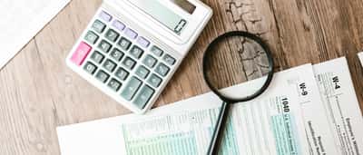 A magnifying glass and a calculator resting on top of U.S. individual income tax forms on a wooden desk.
