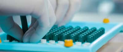 Gloved hands carefully arranging green pharmaceutical capsules in a bright, modern laboratory setting.