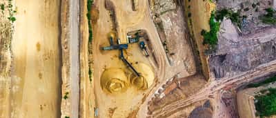 An aerial view of heavy machinery operating in a sandy open-pit mine.