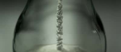 A stream of fine white powder falls into the base of a clear glass container.