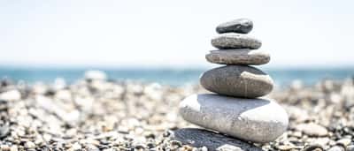 Smooth stones of varying sizes are carefully balanced in a vertical stack on a bright pebble beach.