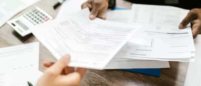 Two professionals exchange paperwork across a desk next to a calculator.