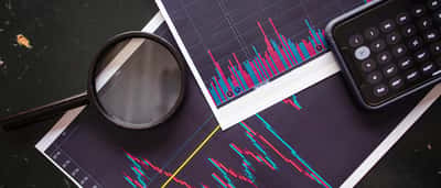 A magnifying glass and a smartphone calculator rest on printed stock market charts.