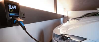 A white electric vehicle is plugged into a charging station in a modern indoor facility.