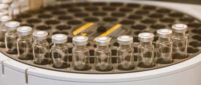 A close-up of glass sample vials arranged in a circular automated testing carousel in a pharmaceutical laboratory.