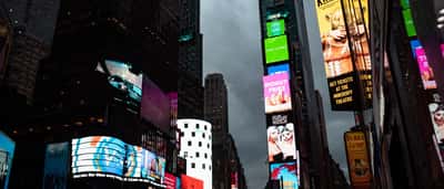 The iconic cylindrical Nasdaq MarketSite building illuminated among the vibrant billboards of Times Square in New York City.
