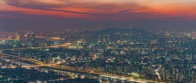 A sprawling aerial view of the Seoul city skyline illuminated at dusk under a dramatic, colorful sunset sky.