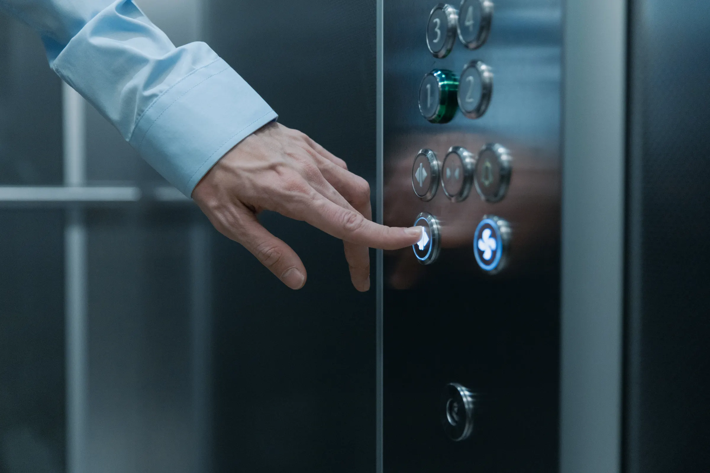 A business professional's hand pressing an illuminated button on a modern elevator control panel.