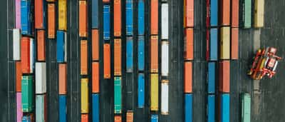 A top-down aerial view of vibrant, multi-colored shipping containers organized in neat rows at a logistics terminal.