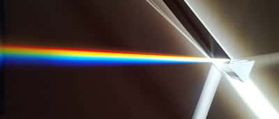 A beam of white light strikes a triangular glass prism and splits into a bright, colorful rainbow spectrum.