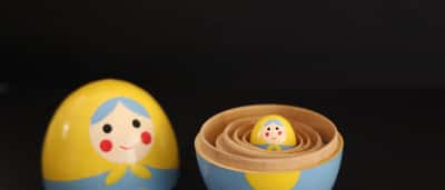 A small yellow and blue wooden nesting doll sits inside the opened base of a larger matching doll against a black background.