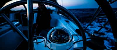 A glowing marine compass mounted on the steering binnacle of a sailboat navigating at twilight.