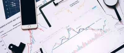 A top-down view of a desk displaying a smartphone, magnifying glass, and printed financial charts analyzing S&P 500 and Nasdaq market returns.