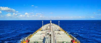 A first-person view from the bow of a large shipping tanker navigating across a bright blue ocean.