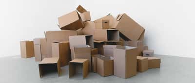 A large pile of plain, empty cardboard boxes of various sizes stacked in a bright, minimalist space.