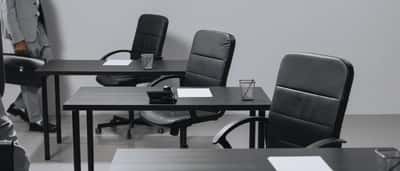 Empty black chairs and desks in a stark, desaturated corporate office setting.