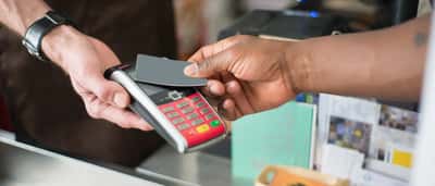 A customer taps a credit card on a payment terminal held by a service worker wearing an apron.