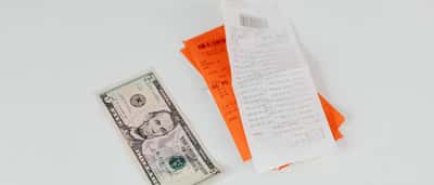 A five-dollar bill lies next to multiple printed shopping receipts on a light surface.