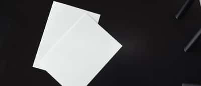 Two blank sheets of white paper lie side-by-side on a dark surface.