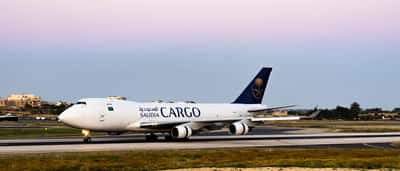 A white Saudia Cargo airplane taxis on an airport runway at twilight.