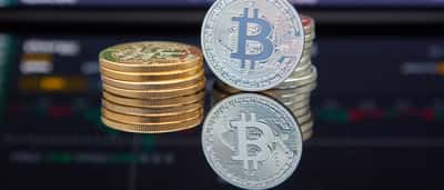 Gold Bitcoin tokens stacked in front of a digital financial trading chart.