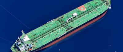 An aerial view of a massive green oil tanker sailing through deep blue ocean waters.
