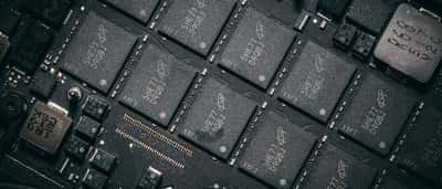 A close-up view of multiple black microchips aligned on a dark electronic circuit board.