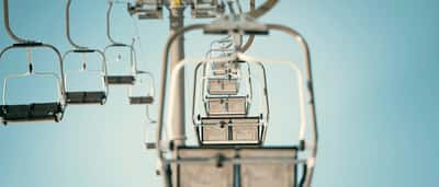A row of empty ski lift chairs ascending into the sky.
