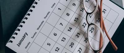 A close-up view of eyeglasses resting on a desk calendar.