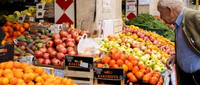 An older man looks at a display of fresh fruit at an outdoor market in Italy.