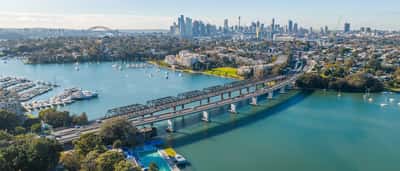 An aerial view of the Sydney skyline, harbor, and bridges on a bright sunny day.