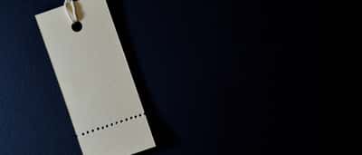 A minimalist blank white tag hangs by a string against a dark background.