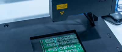 Close-up of an automated inspection machine working on a green printed circuit board in a manufacturing facility.