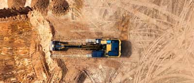 An aerial top-down view of a yellow excavator working on a sandy construction site.