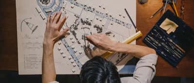 An overhead view of an architect using a compass and ruler to measure a detailed site blueprint.