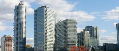 The large red Pepsi-Cola sign stands along a waterfront in front of modern high-rise buildings.
