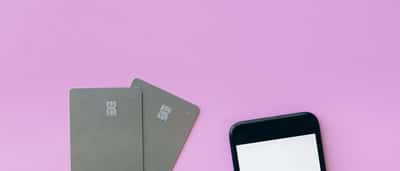 Two minimalist smart cards and a smartphone resting on a vibrant pink background.