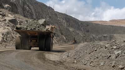 A large yellow mining truck transports rock through a sprawling open-pit quarry.