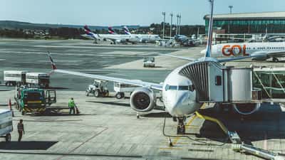 A commercial Boeing 737 MAX airplane parked at an airport gate while ground crew and vehicles prepare it for its next flight.