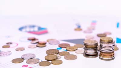 A neat stack of coins resting on printed financial charts and data.