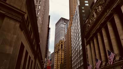 The classic facade of the New York Stock Exchange building stands alongside towering skyscrapers in the dense urban canyon of Wall Street.