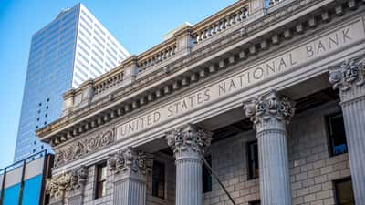 A historic financial building with classical stone columns standing against a clear blue sky.