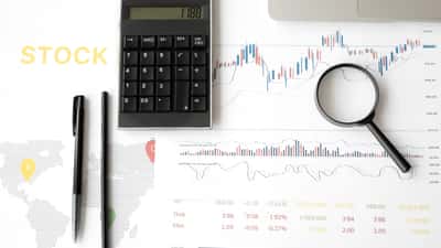 A flat lay of a desk featuring financial line charts, a dotted world map graphic, a calculator, and a magnifying glass.