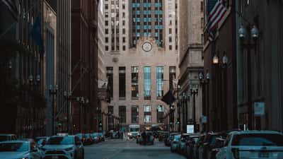 The historic facade of the Chicago Board of Trade building viewed down the center of a busy urban canyon.